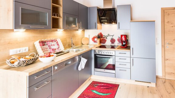 A modern kitchen with gray cabinets and wooden shelves. It is brightly lit and decorated with a red carpet. - Haus Edmund - Sölden