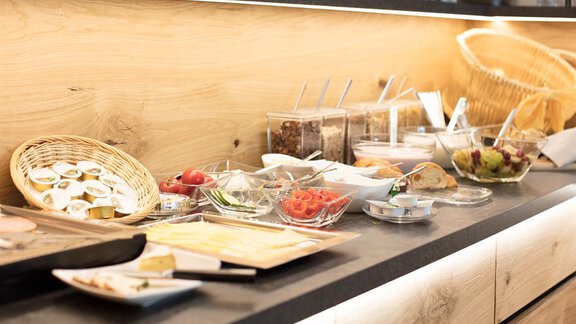 A stylish buffet with various dishes and fresh ingredients. There are fruits, yogurt, muesli, and bread in attractive bowls and baskets. - Haus Gondelblick - Sölden | © Falkner Georg