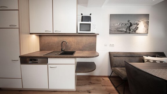 A modern kitchen with white cabinets and an elegant countertop. Next to the kitchen corner, there is a cozy dining area. - Haus Gondelblick - Sölden | © Falkner Georg