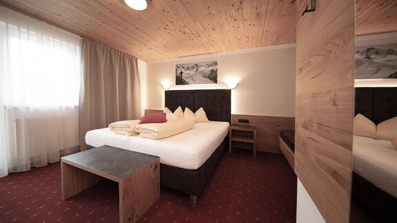 A modern hotel room with a double bed and wooden paneling. The room is bright and cheerful, featuring a cozy seating area and large windows. - Haus Gondelblick - Sölden | © Falkner Georg