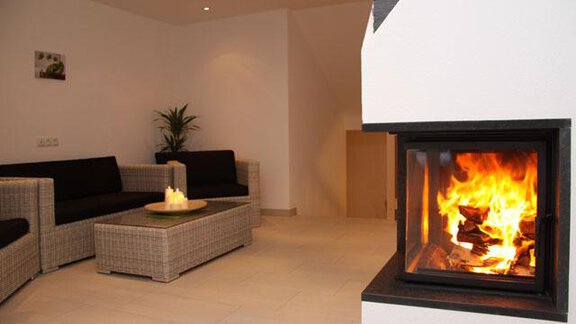 A modern living room with cozy rattan furniture and an elegant fireplace. The flaming logs create a warm and inviting atmosphere. - Haus Ingrid - Sölden