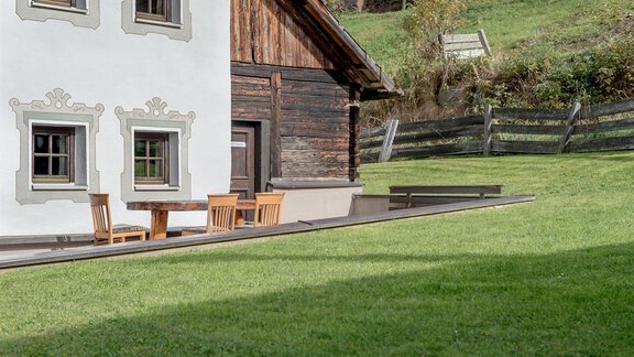 A traditional building with a white facade and wooden elements. In front of the house are wooden furniture on a green lawn. - Landhaus Peater's Hoamat - Sölden