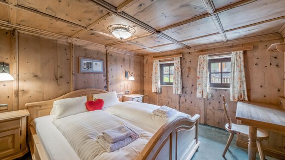A cozy bedroom with wood paneling and two beds. Bright curtains and a warmly lit ceiling create an inviting atmosphere. - Landhaus Peater's Hoamat - Sölden