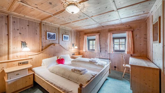 A cozy bedroom with wooden walls and two single beds. The room is bright and friendly, with windows and decorative pictures. - Landhaus Peater's Hoamat - Sölden