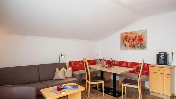 A cozy living area with a sofa and a dining table. The walls are light, and there is decoration with floral motifs. - Sportpension Rubin - Sölden