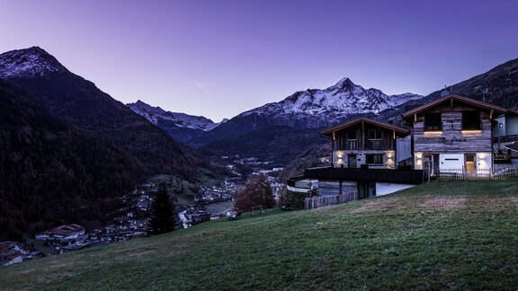 A picturesque valley with snow-capped mountains in the background. In the foreground, there are two wooden chalets on a green meadow. - The Peak Sölden - Sölden