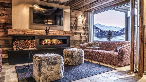 A cozy living space with a modern fireplace and a large window that offers a view of the snow-capped mountains. The decor is rustic and inviting, with a soft rug and stylish furniture. - The Peak Sölden - Sölden