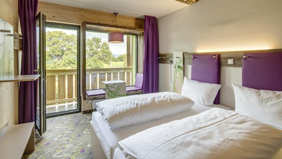 Ein modernes Hotelzimmer mit zwei Betten und eleganter Einrichtung. Der Raum hat einen Balkon und großen Fenstern mit Blick auf die Natur. - Explorer Hotel Ötztal - Umhausen | © Explorer Hotels