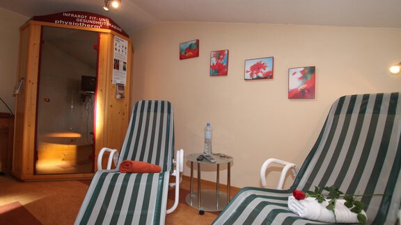 A relaxing wellness room with two lounge chairs and a sauna. Pictures hang on the wall, and on a table are a water bottle and a rose. - Gästehaus Edelweiss - Vent