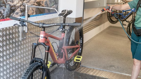 A bicycle is being cleaned at a washing station. The user sprays water on the bike to remove dirt. - Garni Ötztal ROOMS & APARTS - Zwieselstein
