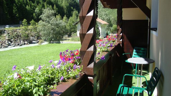 A balcony with colorful flowers and two chairs. In the background, green trees and a meadow can be seen. - Haus Sonnschein - Zwieselstein
