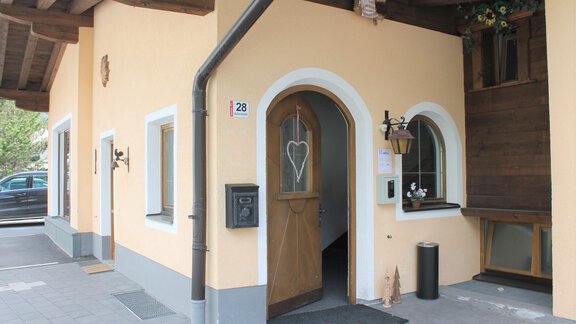 A modern building with an inviting entrance door. The facade is in a warm yellow tone and is sheltered by an awning. - A CASA Appartements Juwel - Sölden