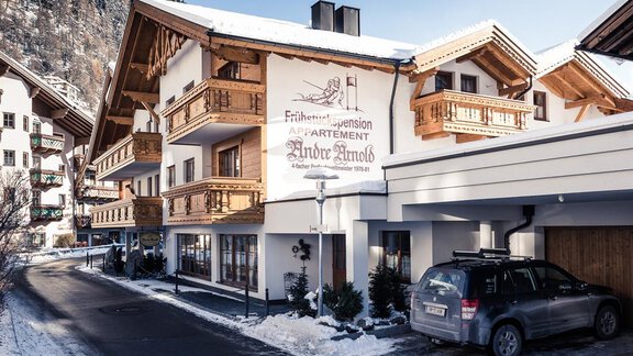 A beautiful chalet with traditional architecture in a snow-covered environment. It features an apartment building with balconies and a large sign. - Andre Arnold - Boutique Hotel - Sölden | © Rudi Wyhlidal