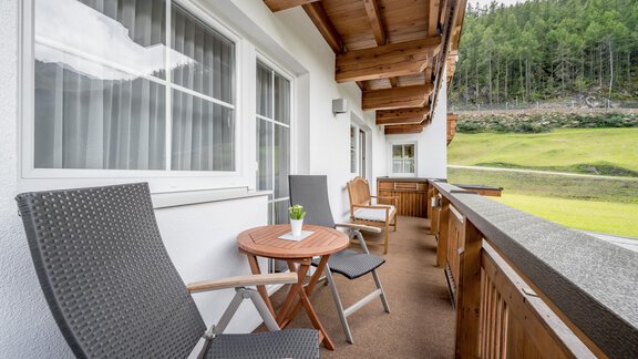 A cozy balcony with two chairs and a small table. In the background, a green meadow and trees. - Appartementhaus Kathrin - Sölden
