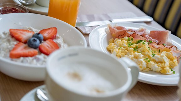 A delicious breakfast with scrambled eggs, ham, yogurt with fruit, and a glass of orange juice. In the background, you can see a cup of coffee. - Appartementhaus Kathrin - Sölden