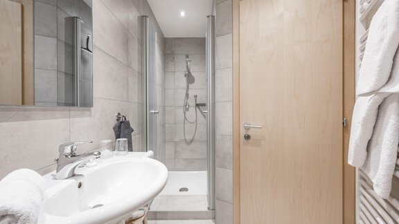 A modern bathroom with a shower and a sink. The walls are painted in a light, neutral color. - Appartementhaus Kathrin - Sölden
