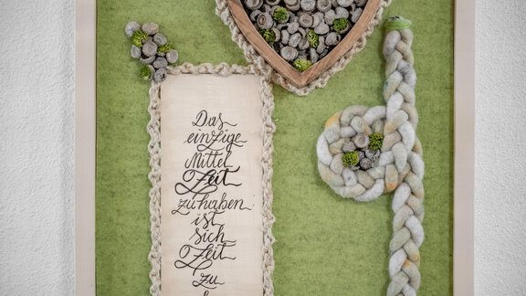 An artistic mural with a green background color. It features calligraphic writing and decorative elements made of natural materials. - Appartementhaus Kathrin - Sölden