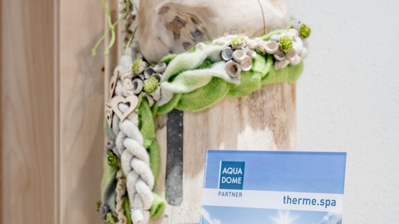 A decorative wooden object with green and white decorations stands on a table. Next to it are informational materials for a spa. - Appartementhaus Kathrin - Sölden