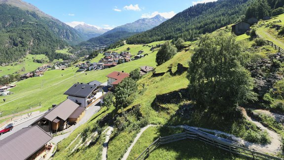 A picturesque landscape with green meadows and mountains in the background. Small houses are scattered in the valley under a bright blue sky. - Belledonne Ski in & out Appartements - Sölden