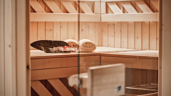 A relaxing sauna room with wood-paneled walls. Towels and a decorative bowl are on the bench. - Belledonne Ski in & out Appartements - Sölden