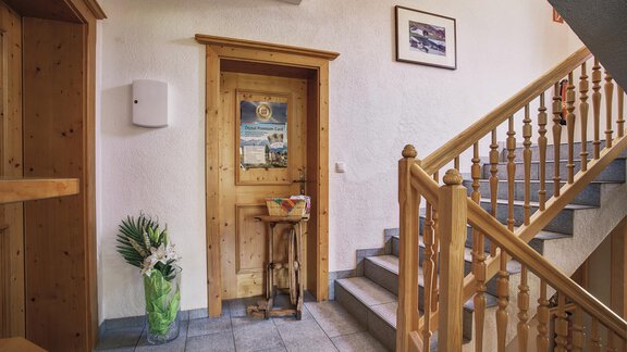 An inviting hallway with a wooden staircase and a decorative door. Pictures hang on the wall, and a plant stands in the corner. - Belledonne Ski in & out Appartements - Sölden