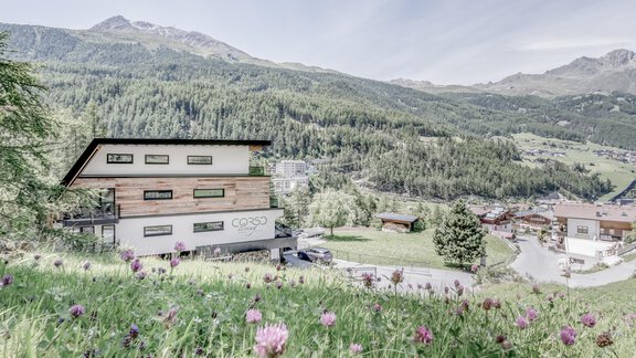 A modern house in a picturesque mountain landscape. Surrounded by green meadows and mountains, with colorful flowers in the foreground. - CORSO living Aparthotel - Sölden