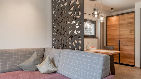 A modern living room with a stylish partition wall and a cozy couch. The dining area is designed in a minimalist and warm style. - CORSO living Aparthotel - Sölden