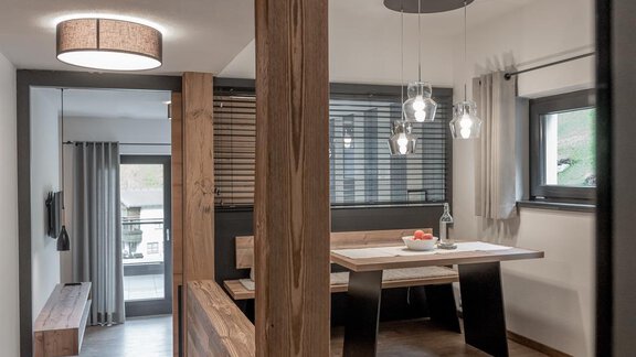 A modernly furnished dining area with a large wooden table and stylish lamps. The large window front lets in plenty of daylight. - CORSO living Aparthotel - Sölden