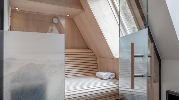 A modern sauna room with wooden paneling and large windows. Fresh towels are available on the benches for use. - CORSO living Aparthotel - Sölden