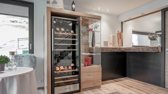 A modern wine storage display made of wood with a glass front is visible in the room. The adjacent area features an elegant bar and a bright, inviting style. - CORSO living Aparthotel - Sölden