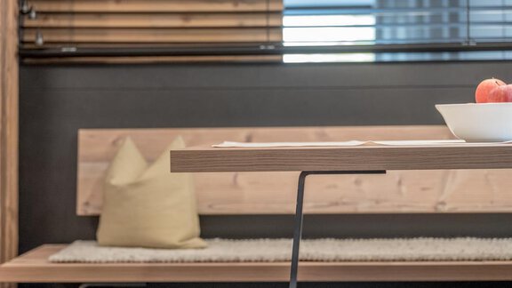 A modern dining area with a wooden table and bench. On the table is a bowl with an apple. - CORSO living Aparthotel - Sölden