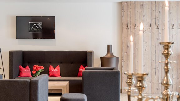 A modern living room with comfortable furniture and stylish decorations. On a table, there are candles and a flower vase, while a television hangs on the wall. - Hotel-Appartements A CASA "Saphir" - Sölden