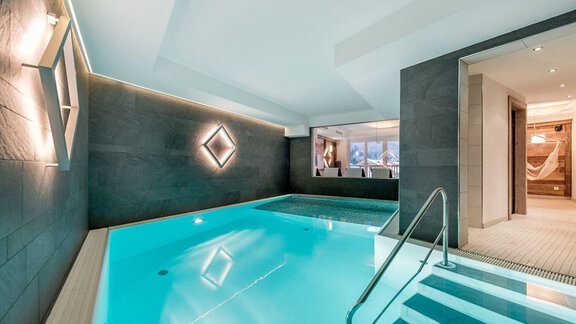 An elegant indoor pool with clear, blue water. The modern architecture and gentle lighting create a relaxing atmosphere. - Hotel-Appartements A CASA "Saphir" - Sölden