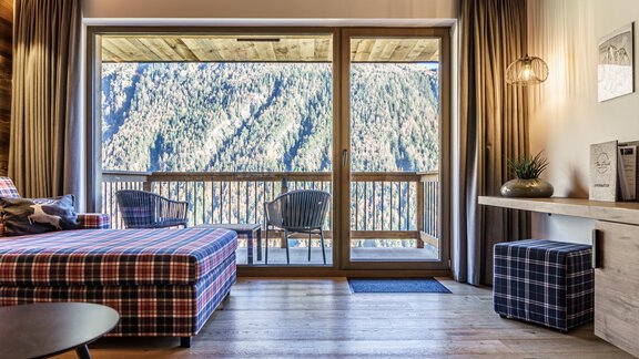A cozy room with a large window that offers a view of the mountains. The room is modernly furnished with a checked sofa and wood-paneled walls. - The Peak Sölden - Sölden