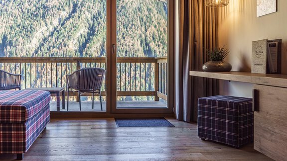 A cozy room with wooden floor and access to a balcony. In the background, tall mountains and a tranquil atmosphere can be seen. - The Peak Sölden - Sölden