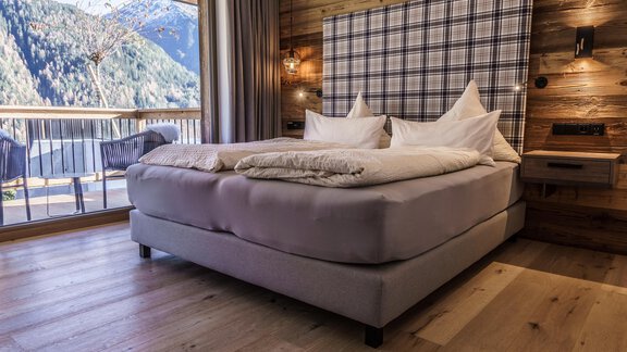 A cozy bedroom with a large bed and a stylish headboard. There is a view of the mountains through the window. - The Peak Sölden - Sölden