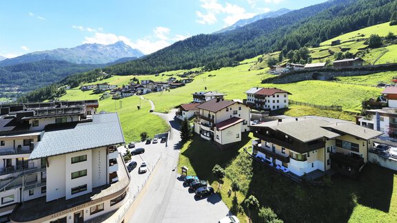 A picturesque landscape with green meadows and mountainsides. In the foreground, several houses and a road can be seen. - A CASA Appartements Juwel - Sölden