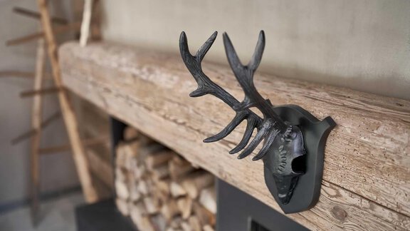 A stylish antler is attached to a wooden panel. In the background, there are wooden logs and a rustic aesthetic. - The Peak Sölden - Sölden