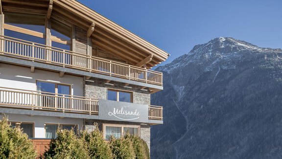 A modern building with wooden cladding and a balcony in a mountainous setting. In the background, a snow-covered peak can be seen. - The Peak Sölden - Sölden