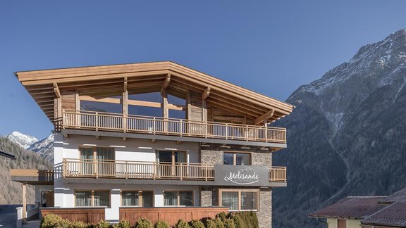 A modern chalet with wood cladding and large windows. Majestic mountains can be seen in the background. - The Peak Sölden - Sölden