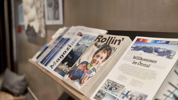 A series of magazines is lying on a shelf. The titles showcase various themes, including leisure and travel magazines. - The Peak Sölden - Sölden