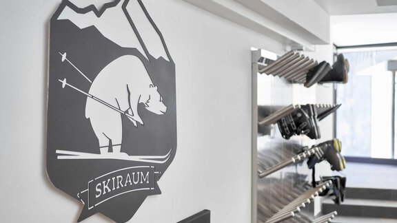 A sign featuring a bear skiing hangs on the wall. In the background, ski equipment racks can be seen. - The Peak Sölden - Sölden