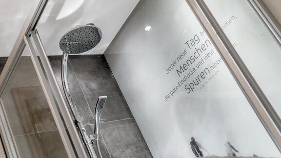 A modern shower with a large rain shower head and glass walls. On the wall, there is an inspiring quote about life. - The Peak Sölden - Sölden