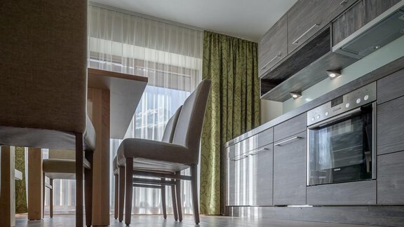 A modern kitchen with wooden cabinets and a stove. Next to it is a wooden dining table with chairs. - The Peak Sölden - Sölden