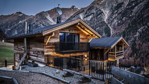 A modern wooden house in the mountains, surrounded by high peaks. It has large windows and a balcony with a view of the landscape. - The Peak Sölden - Sölden