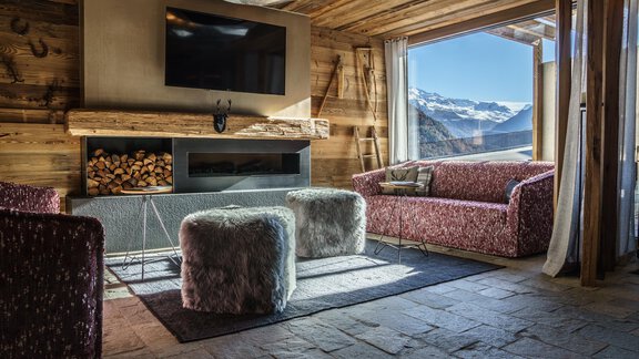 A cozy living room with wooden furniture and a modern television. Large windows offer a view of the mountains. - The Peak Sölden - Sölden