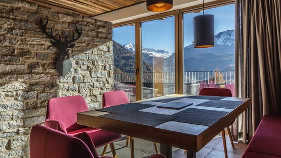 A modern dining room with a wooden table and pink chairs. Large windows offer a view of the mountains and nature. - The Peak Sölden - Sölden