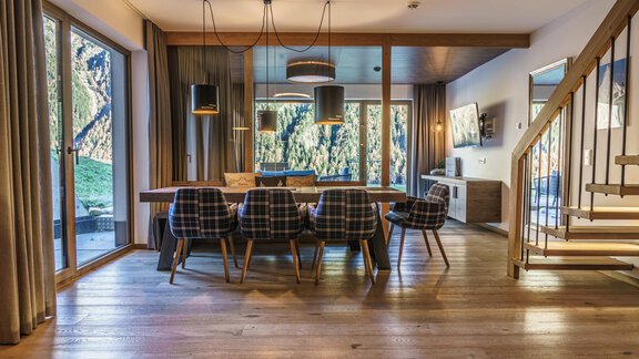 A modern dining room with a large table and stylish chairs. Large windows offer a view of nature and plenty of natural light. - The Peak Sölden - Sölden