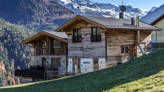 A modern wooden mountain cabin with a beautiful view of the surrounding mountains. In the background, colorful forests can be seen. - The Peak Sölden - Sölden