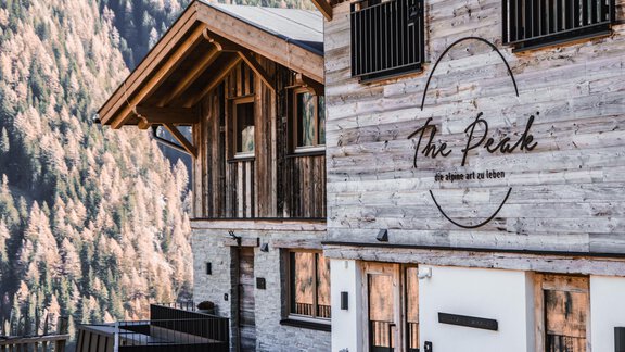 A modern wooden building with an inviting sign "The Peak". The surroundings are characterized by majestic mountains and trees. - The Peak Sölden - Sölden